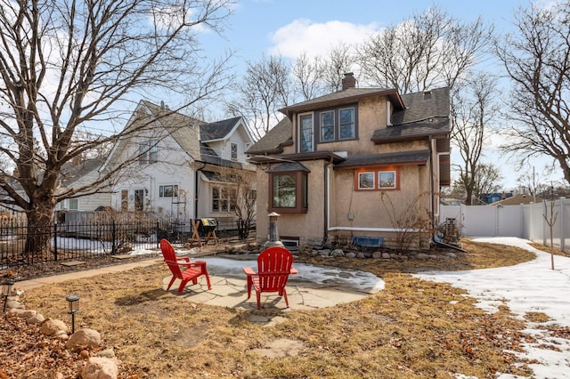 snow covered house featuring a fenced backyard, stucco siding, a chimney, and a patio