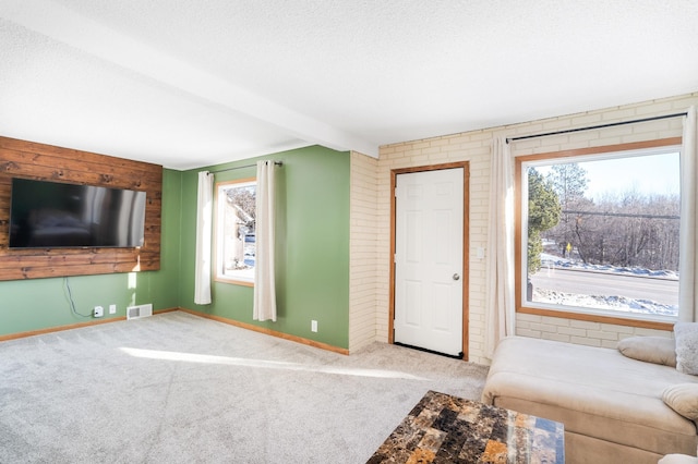 unfurnished living room with a textured ceiling, light colored carpet, brick wall, and beam ceiling