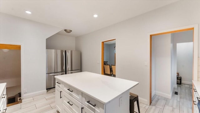 kitchen with white cabinetry, baseboards, light countertops, freestanding refrigerator, and a center island