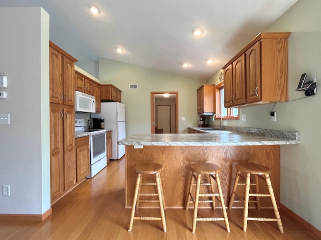 kitchen with a peninsula, a sink, lofted ceiling, white appliances, and a breakfast bar