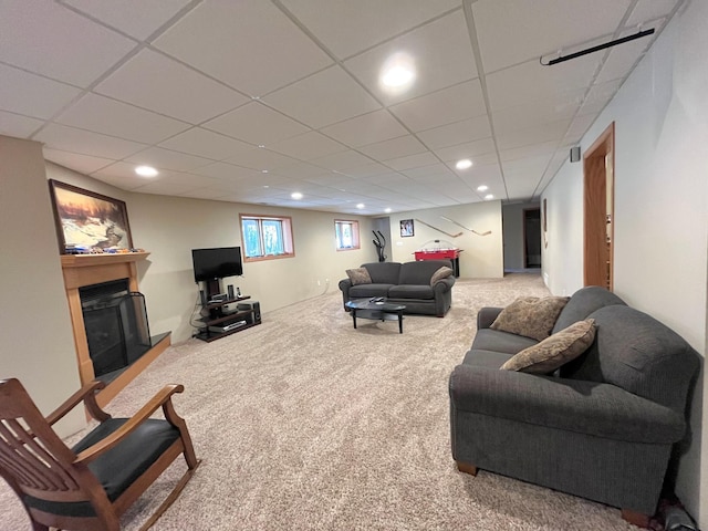 living room with carpet flooring, a drop ceiling, a fireplace with raised hearth, and recessed lighting