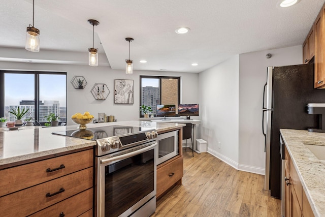 kitchen with brown cabinetry, appliances with stainless steel finishes, decorative light fixtures, light stone countertops, and a view of city