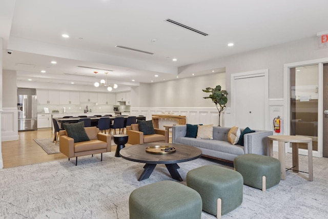 living room featuring a wainscoted wall, light wood finished floors, recessed lighting, visible vents, and a decorative wall