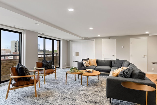 living room featuring light wood finished floors, baseboards, a city view, floor to ceiling windows, and recessed lighting