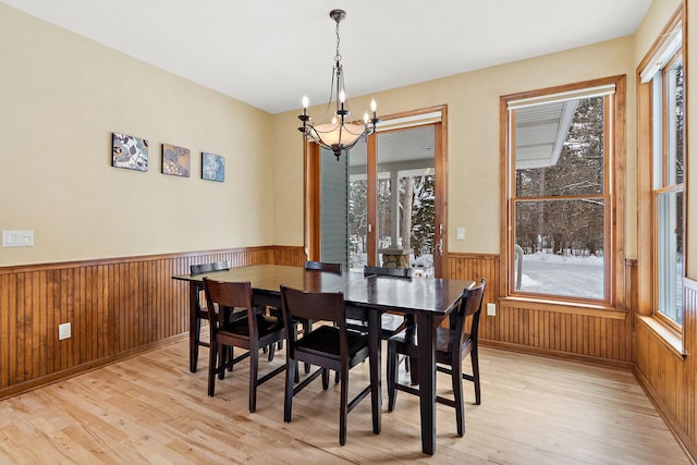 dining area featuring wood walls, a chandelier, light wood finished floors, and wainscoting