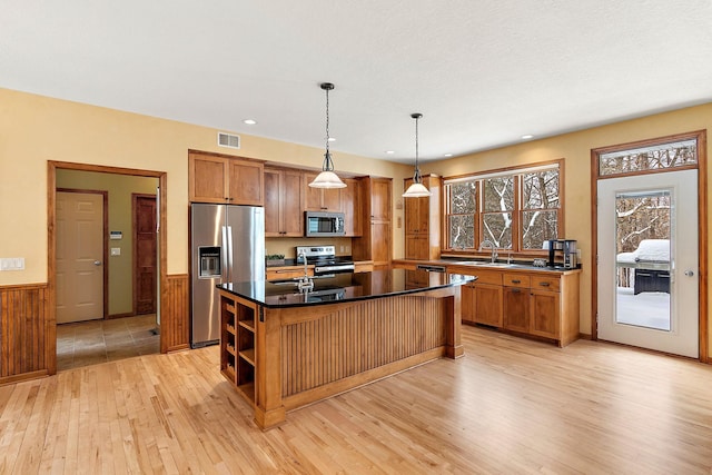 kitchen featuring pendant lighting, brown cabinets, stainless steel appliances, dark countertops, and a kitchen island