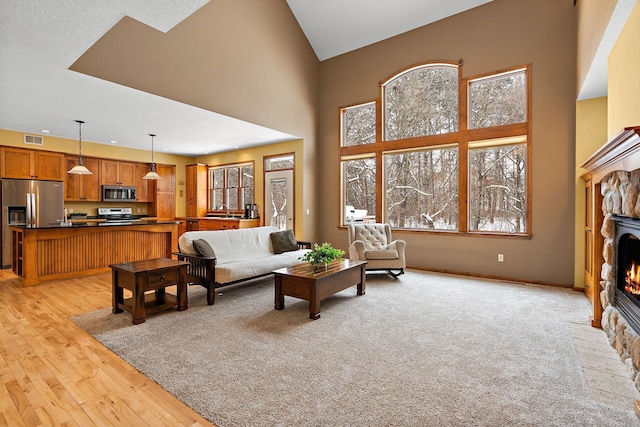 living area with light wood finished floors, visible vents, baseboards, a fireplace, and high vaulted ceiling