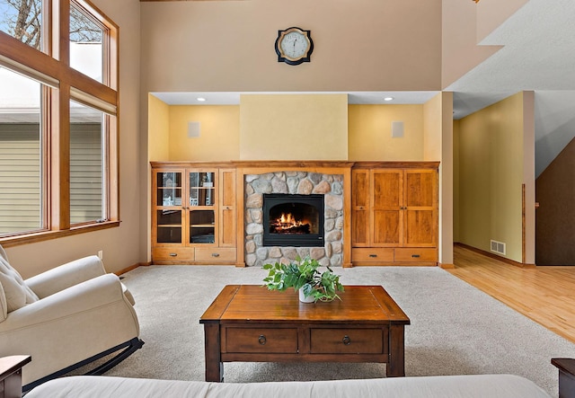 living area featuring visible vents, a high ceiling, carpet, a fireplace, and baseboards