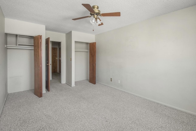 unfurnished bedroom with ceiling fan, multiple closets, carpet floors, and a textured ceiling