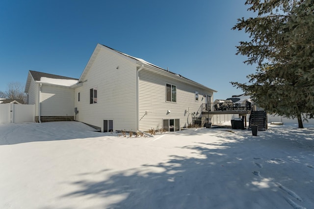 snow covered property with a wooden deck, stairs, and fence