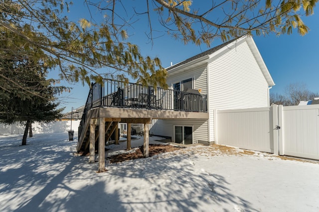 snow covered property with a deck, stairway, a gate, and fence