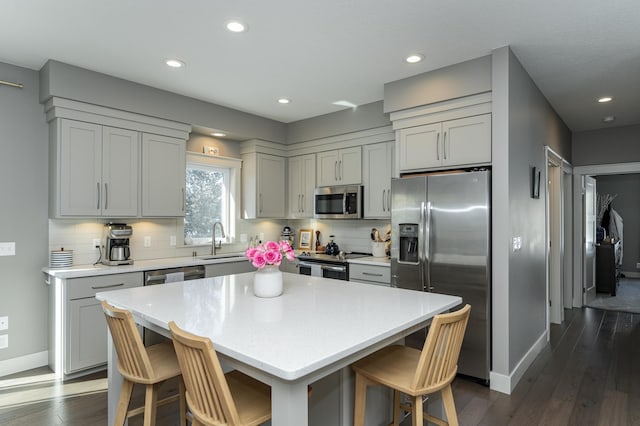 kitchen featuring dark wood finished floors, a kitchen bar, decorative backsplash, stainless steel appliances, and a sink