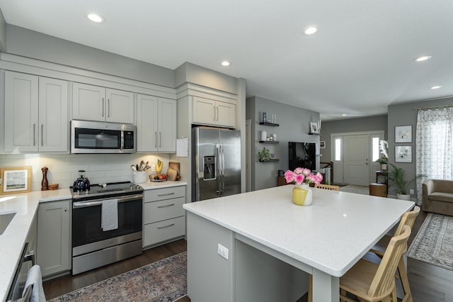 kitchen featuring dark wood-type flooring, open floor plan, decorative backsplash, gray cabinets, and appliances with stainless steel finishes