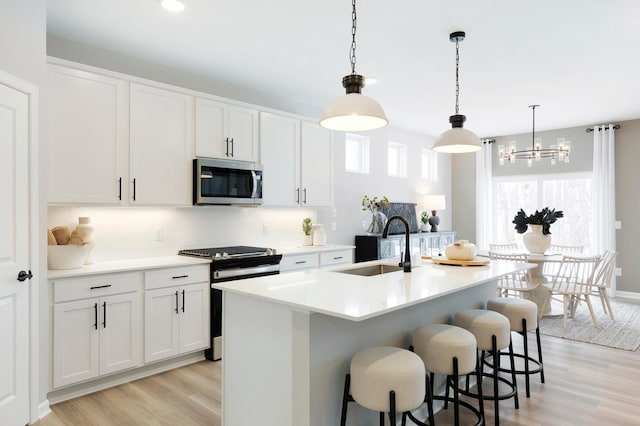 kitchen with range with gas cooktop, white cabinetry, sink, hanging light fixtures, and a kitchen island with sink