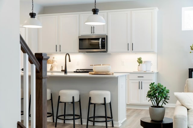 kitchen featuring pendant lighting, sink, white cabinetry, a kitchen breakfast bar, and decorative backsplash