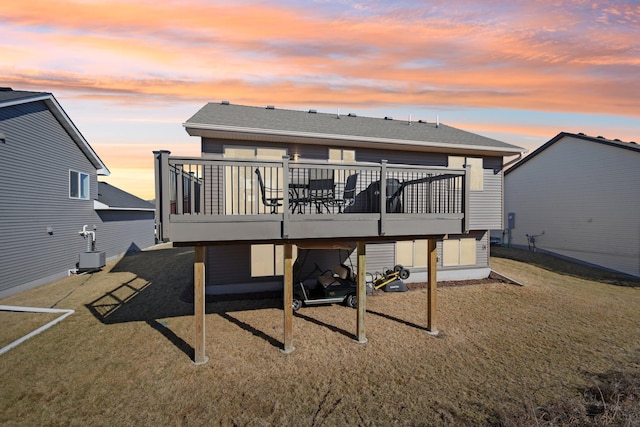 back of house at dusk featuring central AC, a deck, a lawn, and roof with shingles