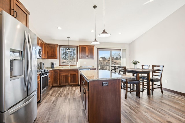 kitchen with light stone counters, pendant lighting, stainless steel appliances, light wood-style floors, and a kitchen island