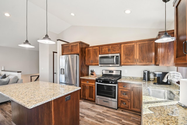 kitchen featuring lofted ceiling, wood finished floors, light stone countertops, stainless steel appliances, and a sink