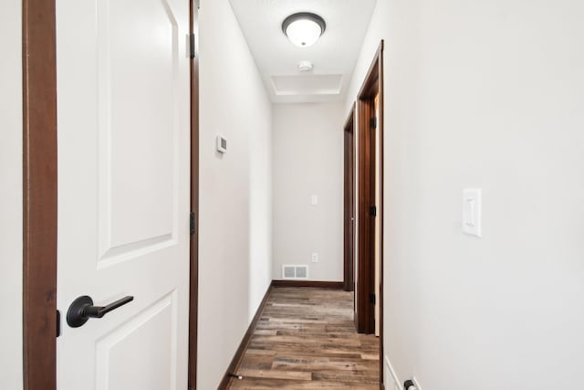 hallway with wood finished floors, visible vents, and baseboards