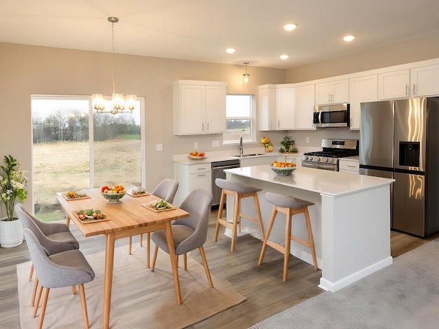 kitchen featuring a chandelier, stainless steel appliances, a sink, white cabinetry, and a center island