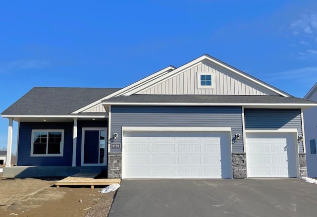 view of front facade with aphalt driveway, stone siding, an attached garage, and board and batten siding