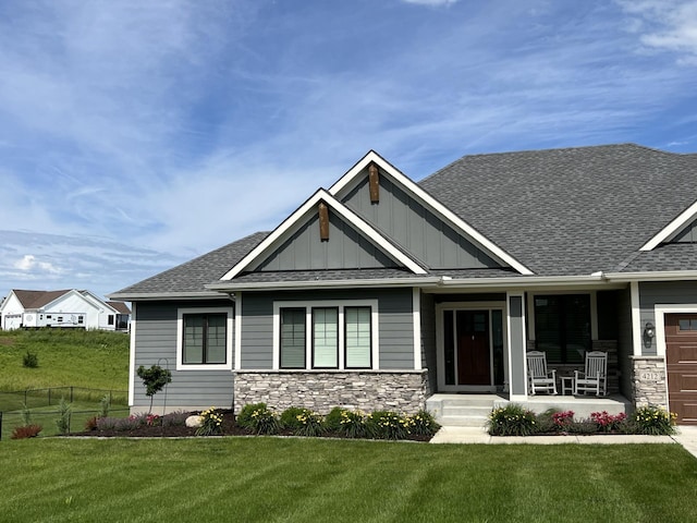 craftsman inspired home with a porch, stone siding, roof with shingles, a front lawn, and board and batten siding