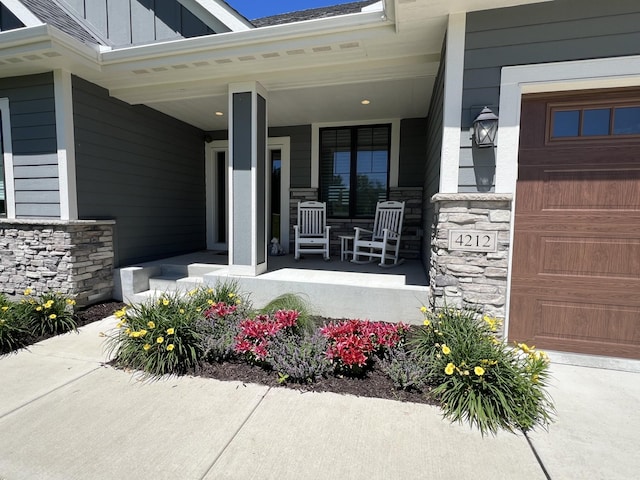 doorway to property with board and batten siding, covered porch, stone siding, and a garage