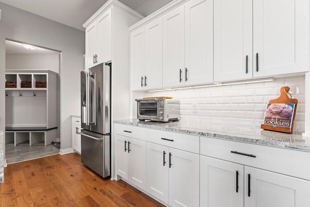 kitchen featuring light stone countertops, decorative backsplash, white cabinetry, wood finished floors, and high end refrigerator