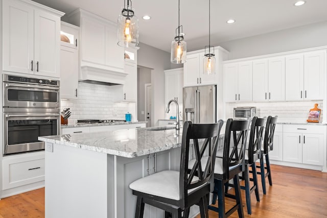 kitchen with a kitchen breakfast bar, stainless steel appliances, a kitchen island with sink, and white cabinetry