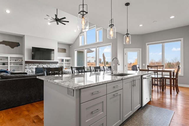 kitchen with open floor plan, light stone countertops, a kitchen island with sink, stainless steel dishwasher, and a sink