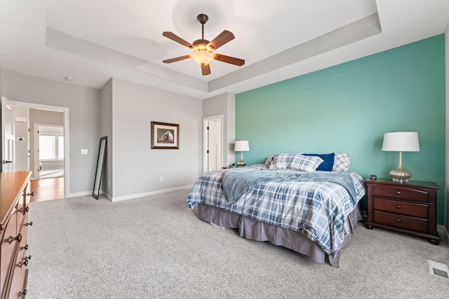 bedroom featuring carpet flooring, a ceiling fan, visible vents, baseboards, and a tray ceiling