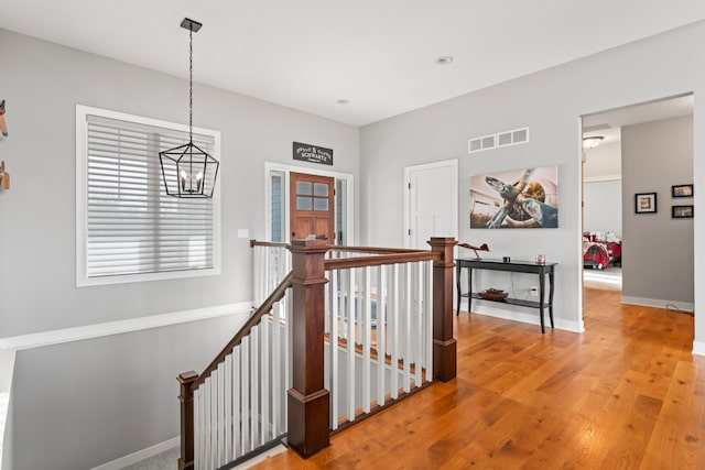 corridor with visible vents, wood finished floors, an upstairs landing, and baseboards