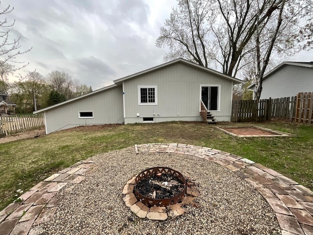 back of property featuring entry steps, a fenced backyard, a lawn, and a fire pit