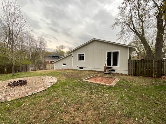 back of house featuring a patio area, a fenced backyard, a yard, a fire pit, and entry steps
