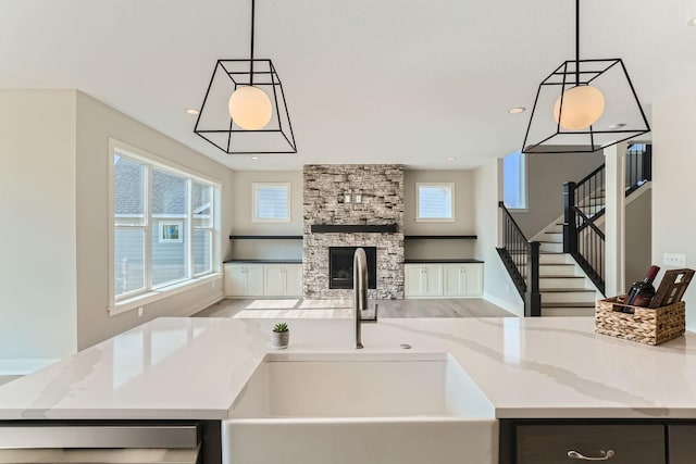 kitchen featuring pendant lighting, light stone counters, a stone fireplace, and dishwashing machine