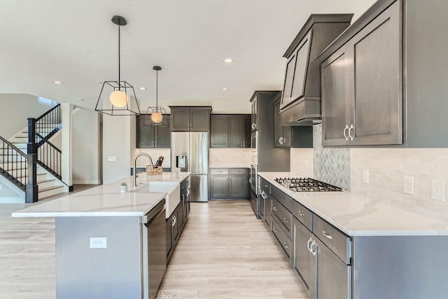 kitchen with pendant lighting, sink, light hardwood / wood-style flooring, appliances with stainless steel finishes, and a kitchen island with sink