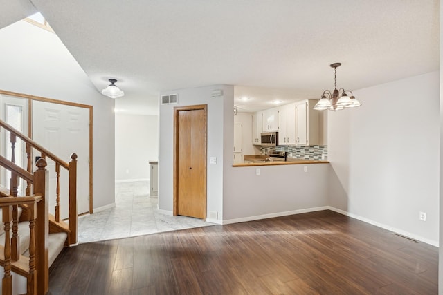 interior space with an inviting chandelier, light wood-style flooring, stairs, and visible vents