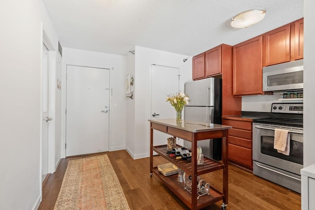 kitchen featuring brown cabinetry, a textured ceiling, stainless steel appliances, and wood finished floors