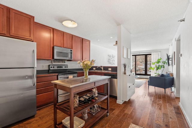 kitchen with a sink, a textured ceiling, dark wood-style floors, appliances with stainless steel finishes, and brown cabinetry