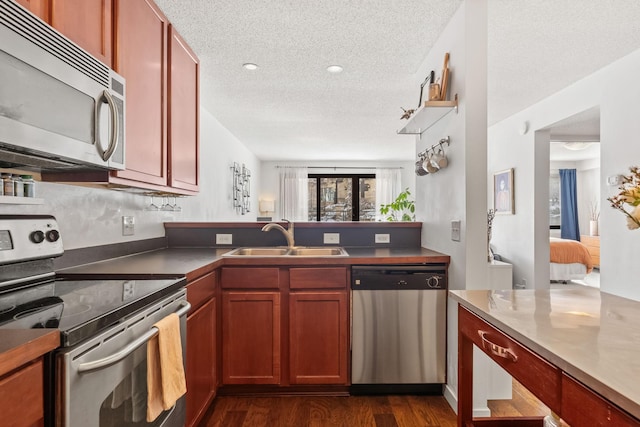 kitchen with a sink, a textured ceiling, dark wood-style floors, appliances with stainless steel finishes, and a peninsula