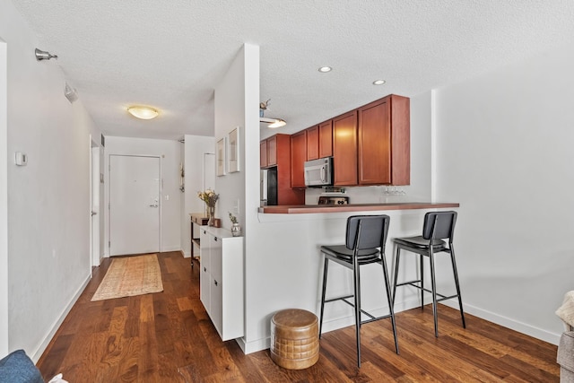 kitchen featuring a kitchen breakfast bar, a textured ceiling, appliances with stainless steel finishes, and dark wood-style floors