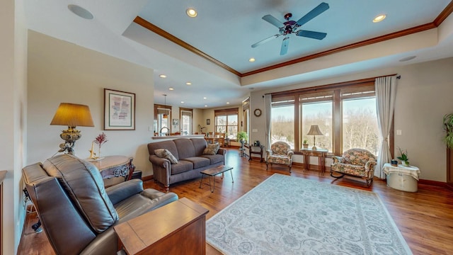 living room with a tray ceiling, ornamental molding, light wood-type flooring, and ceiling fan