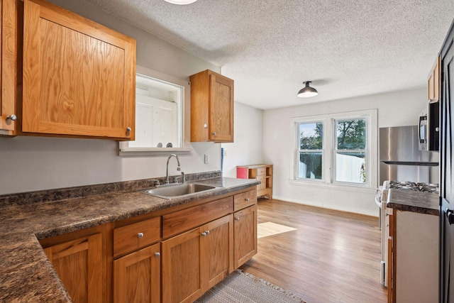 kitchen with a textured ceiling, stainless steel fridge, hardwood / wood-style floors, sink, and range with gas cooktop