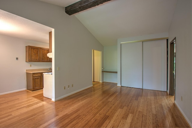 unfurnished bedroom with vaulted ceiling with beams, a closet, baseboards, and light wood-style floors