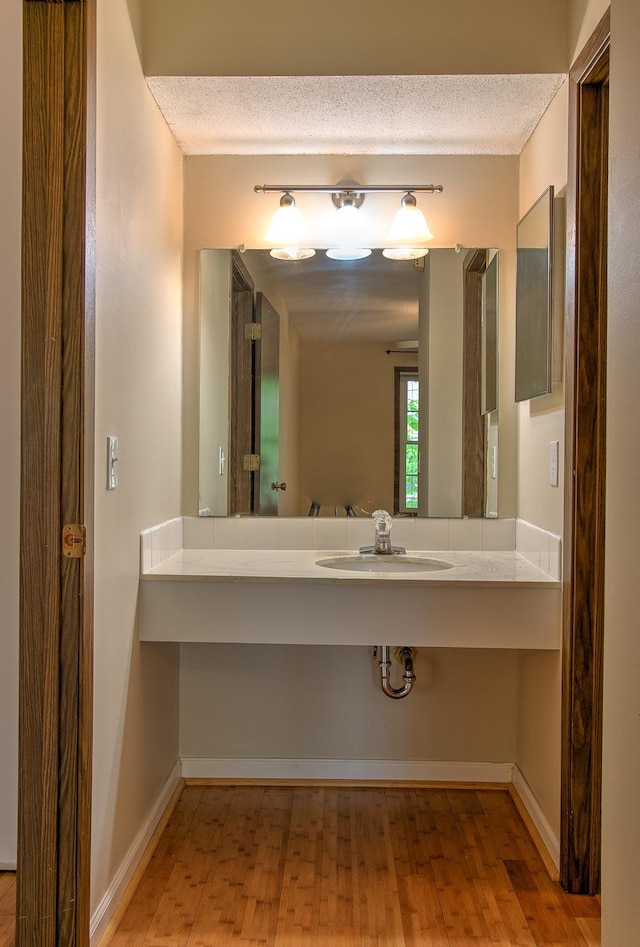 bathroom with a textured ceiling, wood finished floors, a sink, and baseboards