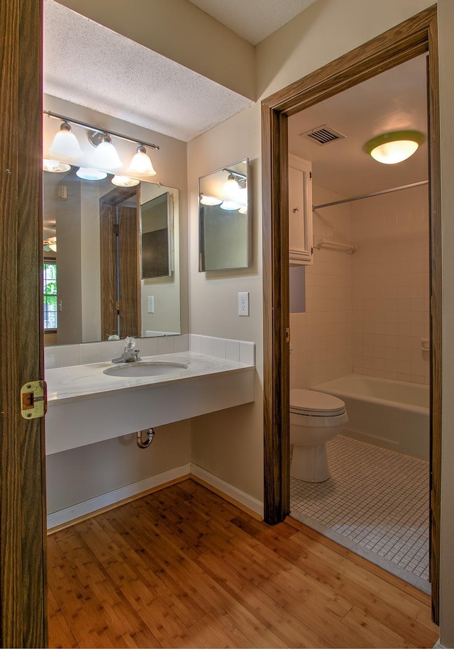 bathroom featuring visible vents, toilet, a sink, a textured ceiling, and wood finished floors