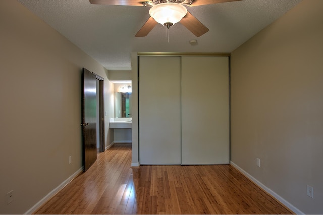 unfurnished bedroom featuring light wood finished floors, baseboards, a ceiling fan, a textured ceiling, and a closet