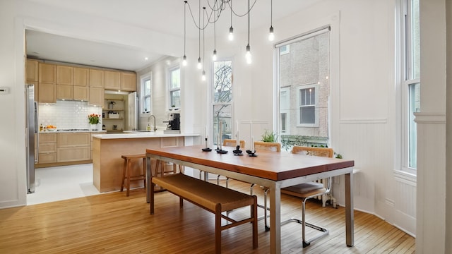 dining area with a decorative wall, light wood-style floors, and wainscoting