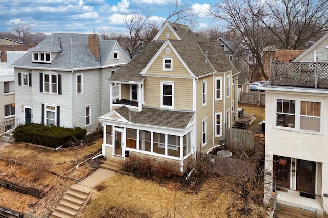 exterior space with fence, a shingled roof, a chimney, and a sunroom