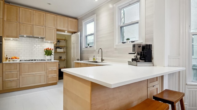 kitchen with a breakfast bar area, light brown cabinets, a peninsula, a sink, and decorative backsplash